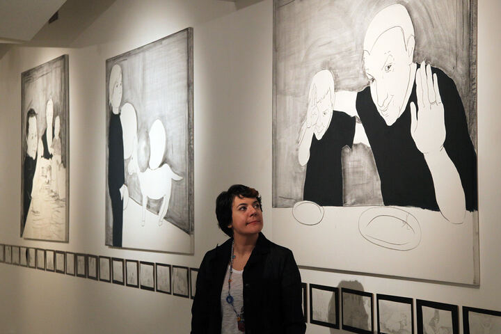 Umjetnica ispred svojih platana u galeriji, ispod niza minijatura